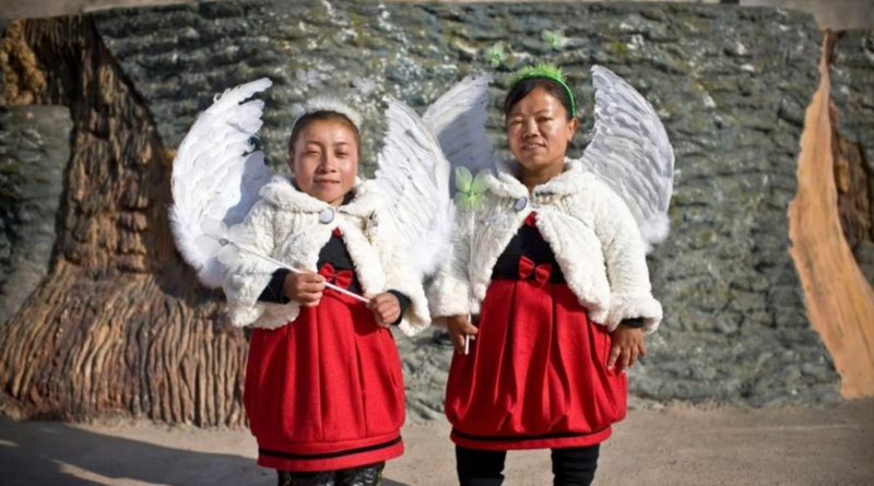 A photograph of two children wearing red dresses, white jackets and angel wings